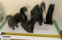 Five soapstone figures and a bone implement displayed on shelf with measuring tape
