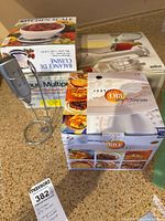 Photo showing boxed kitchen scale, boxed microwave rice cooker, and boxed Braun Multipractic hand blender on countertop.