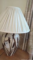 Full view of the ceramic lamp showing the beige pleated fabric shade and the ceramic base with brown reeds design.