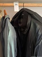 Two men's jackets hanging on a clothing rod, one black leather jacket and one grey raincoat