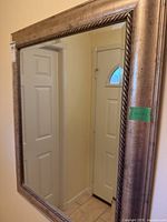 Full view of the wall mirror showing reflections of doors and tiled floor, highlighting overall size and condition.