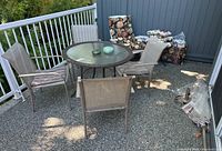 Full view of patio set with round glass-top table, four striped cushioned chairs, floral resin lounge chair with cushions, stacked pillows, side table, folded umbrella and stand on outdoor deck patio.
