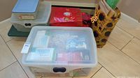 Stacked plastic storage bins on floor with visible contents including boxed decorative lights and wrapping materials