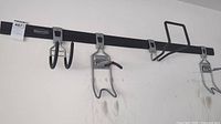 Wide view of Rubbermaid black metal wall rail with five hooks attached, showing various metal hooks for tool hanging with one strap.