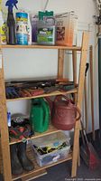 Wooden shelf with garden supplies such as sprays, fertilizers, gloves, watering cans, and boots.