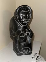 Front view of the soapstone carving figurine depicting a hooded Indigenous person holding an animal with carved facial features.