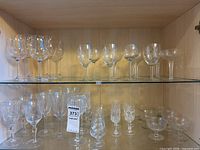 Shelf with various clear glass stemware glasses of different sizes and shapes, including wine glasses, brandy snifters, and sherry glasses