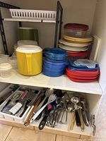 Photo showing stacked plastic storage containers in yellow, blue, white, and red colors; assorted kitchen utensils spread in a tray including metal and wooden-handled items