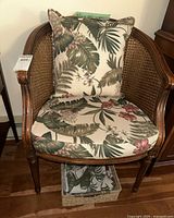 Front view of wicker armchair showing cane sides and back, wooden frame, floral seat cushion and pillow.