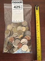 Photo of plastic bag containing assortment of world coins next to measuring tape showing coin sizes up to about 3 cm.