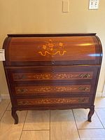 Front view of wooden roll-top desk showing three drawers and floral inlay