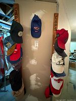 Wide shot showing two wooden wall racks labeled CAPS with multiple baseball caps hung, variety of colors and team logos visible