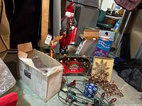 Overview photo showing box with string lights, wooden deer box, plush snowman, framed ornament, and other holiday decorations placed on the floor.