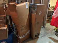 Two large cardboard boxes likely containing Christmas trees in a basement setting.