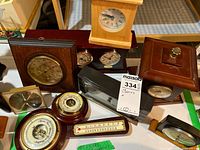 Overview of assorted clocks, barometers, and thermometers with wood and brass features positioned on a table.
