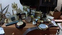 Overview of multiple clocks, thermometers, and parts on wooden table showing varied sizes and styles from small to medium pieces.
