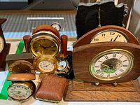 Nine assorted vintage travel and desk clocks including a polished granite clock, wooden clocks, and small leather-covered travel clocks arranged on a table
