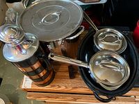 Photo of all cookware including pots with lids, roasting pan, T-Fal grill and copper-stainless steel thermos on a wooden surface