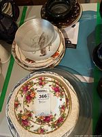 Stack of various plates and bowls with floral and clear glass patterns, including china dishes and clear ribbed glass bowl on top