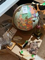 Photo of lot contents showing the colorful globe, cow weathervane atop stand, and various artisan decor items including carved stone horse bookend and key holder.