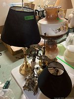 Set of three vintage lamps on table including brass finish lamp with black shade, brass finish lamp without shade, and painted glass floral lamp