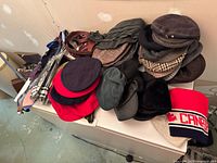 Various men's hats including knitted, wool tams, caps of wool and tweed stacked and laid on a surface showing the collection variety