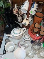 Photo showing mugs, teapot, glasswares, and other kitchen items together on a shelf and table.