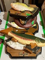 Five musical fish plaques grouped together showing different fish mounted on wooden plaques. Three are Big Mouth Billy Bass, one Wiggling Willie, and one additional fish plaque with a burgundy base.