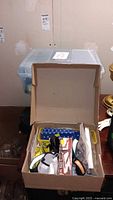 Open cardboard box showing assorted office supplies including pens, microcassettes, and organizers.