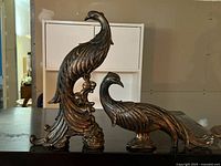 Pair of bronze peacock sculptures with elegant curved tails on display on table in side view