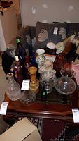 Multiple glass decanters, bottles including cobalt blue and amber, porcelain vase, and various glass vases displayed on wooden table in room