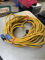 Coiled yellow 100 foot extension cord with blue tape and price tag on one end, displayed on an outdoor table.