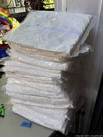 Stack of 22 white disposable hazmat coveralls, each individually sealed in plastic packaging.