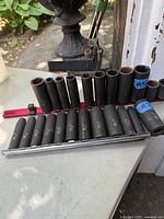 Two sets of black metal sockets, various sizes and styles, arranged on rails, photographed outdoors with garden setting background.