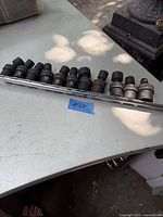 Photo showing 12 black impact sockets on metal rail laid on a table outdoors.