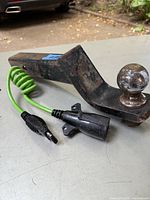 Trailer tow hitch with 2 inch drop ball and attached green electrical hookup cable laid on table with vehicle in background.
