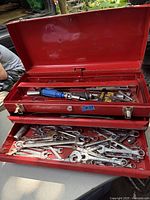 Full view of the open vintage red metal toolbox showing hand tools compartments and drawers with wrenches and screwdriver bits inside.