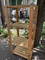 Full image of the wood shelving unit outdoors showing the four slatted shelves and upright wooden supports, natural wood finish.