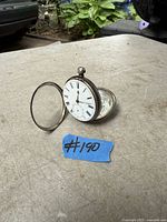 Antique silver pocket watch open showing white dial with black Roman numerals, small seconds dial and metal crown at top.