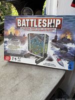 Photo of the Battleship Tactical Combat Game box, showing detailed artwork of naval ships, submarines, and missile combat, with game board in the center.