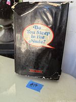 Photo of the book's front cover with the worn black dust jacket and title in speech bubble