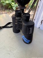 Full view of Bushnell binoculars on a white surface with strap, showing the front and eyepiece sides.