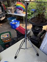 Full view of chrome metal tripod stand with rubber feet, adjustable height with wing screws, and a holder on top for mounting cymbals or drums.