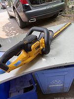 Front angle of cordless DeWALT hedge/edge trimmer placed on table outdoors with handle, blade visible
