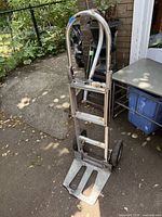 Front view of aluminum dolly hand truck with visible shape, handle, base plate, and wheels.