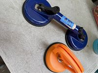 Top-down photo showing the blue double suction cup lifter with two suction cups joined by a metal handle and black lever releases.