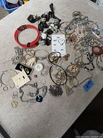 Overview of assorted costume jewelry laid out on a table including necklaces, bracelets, earrings, rings, brooches, pendants, and decorative items such as a white elephant figurine. Various colors and materials visible.