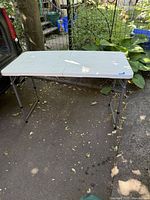 Full side view of the folding table showing the metal legs and white plastic top outdoors.