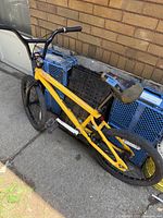 Side profile of the vintage yellow GT BMX bike leaning against blue crates, showing the frame, seat, chain missing, and wheels.