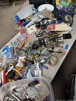 Photo showing assorted small tools and hardware items spread on a table including electrical tape, sockets, screws, and various metal parts.